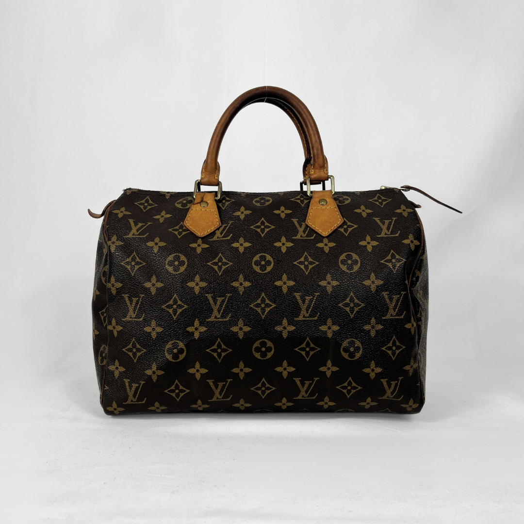 A Louis Vuitton monogram canvas Speedy handbag in dark brown with tan leather handles and trim, photographed against a light gray studio background.