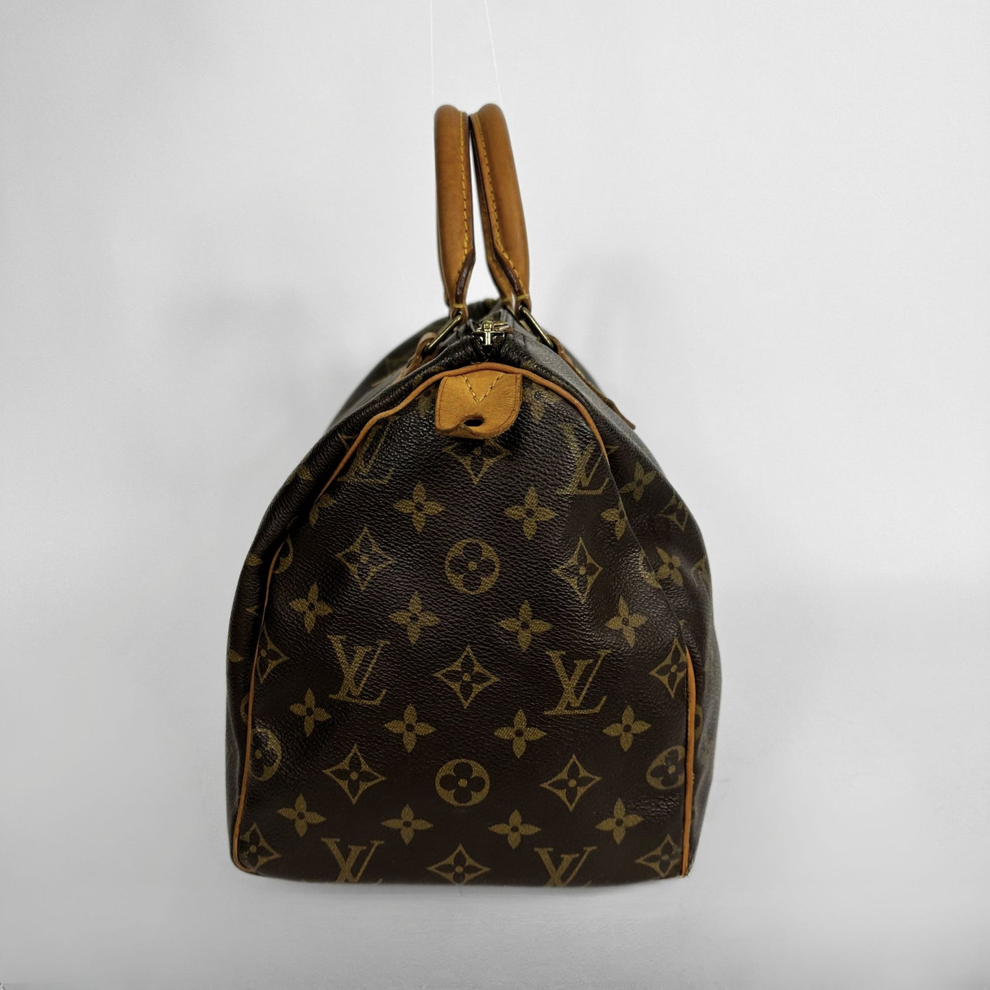 A Louis Vuitton monogram canvas Speedy bag with tan leather handles and trim, photographed against a plain light gray background.