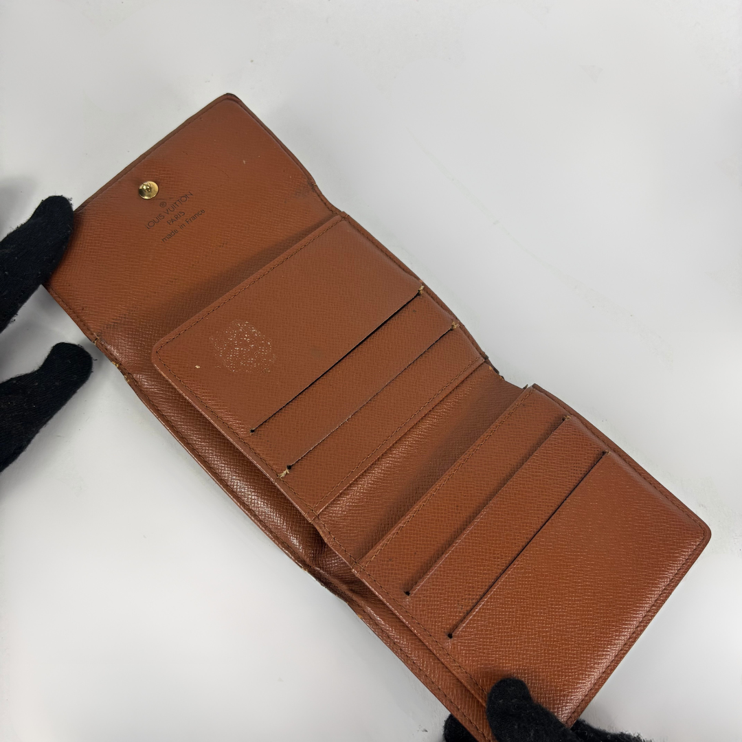 A brown textured leather wallet shown open, held by black-gloved hands against a plain white background.