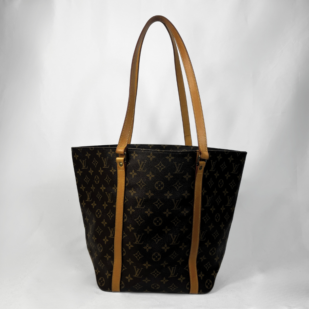 A Louis Vuitton tote bag in black monogram canvas with tan leather shoulder straps and trim, photographed against a light gray studio background.
