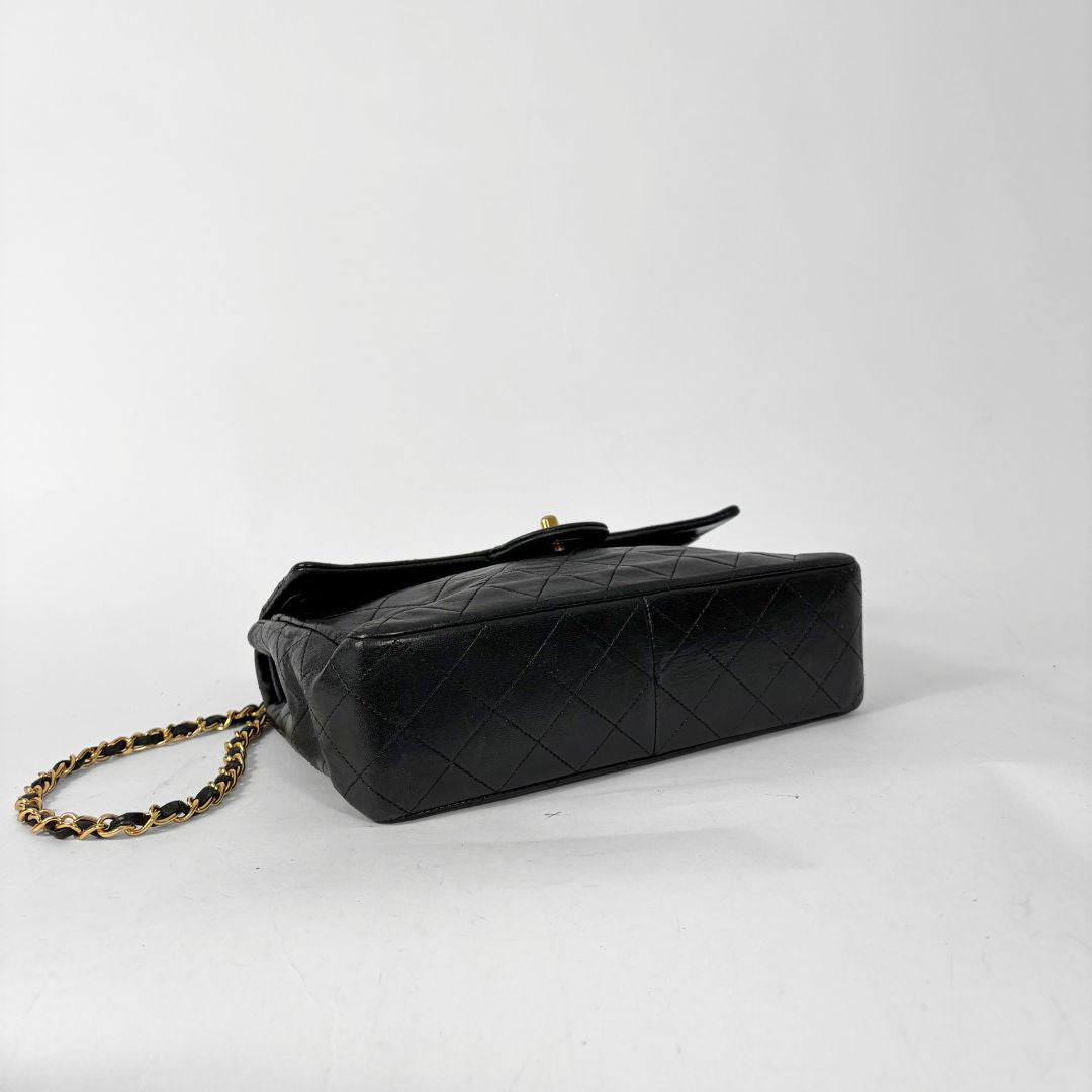 Black quilted handbag with gold chain and clasp on a white background