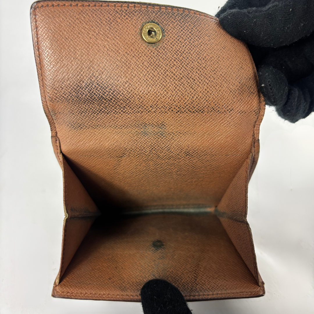 A brown textured leather wallet or card holder shown open, with a black gloved hand holding it against a plain white background.