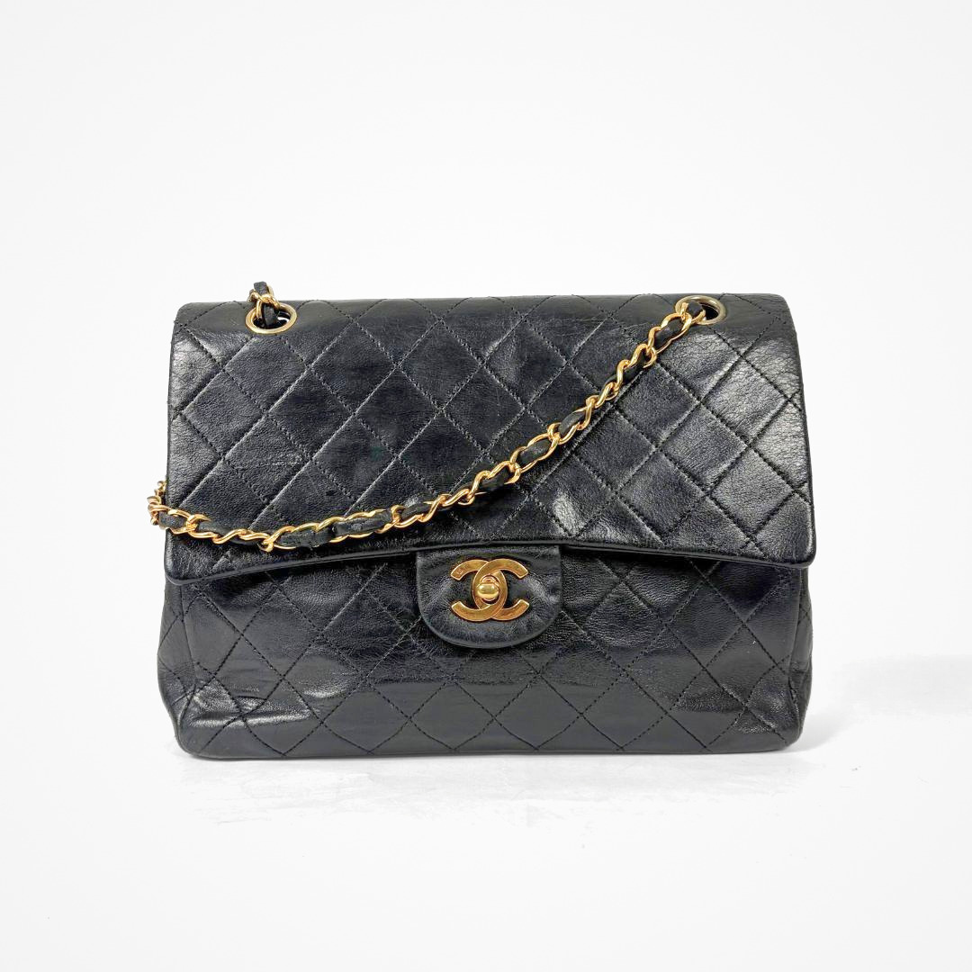 Black Chanel handbag with gold chain and clasp on a white background
