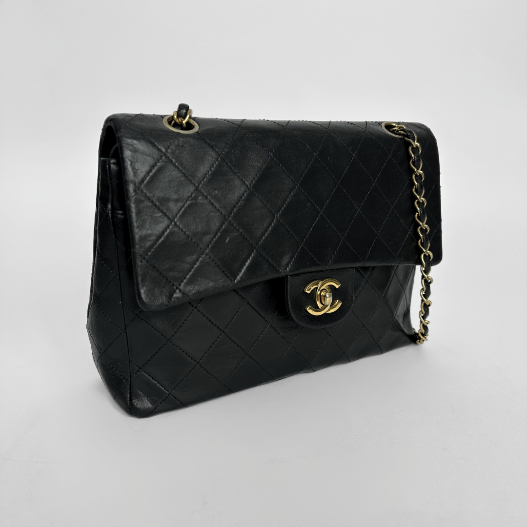 Black quilted handbag with gold chain and clasp on a light gray background