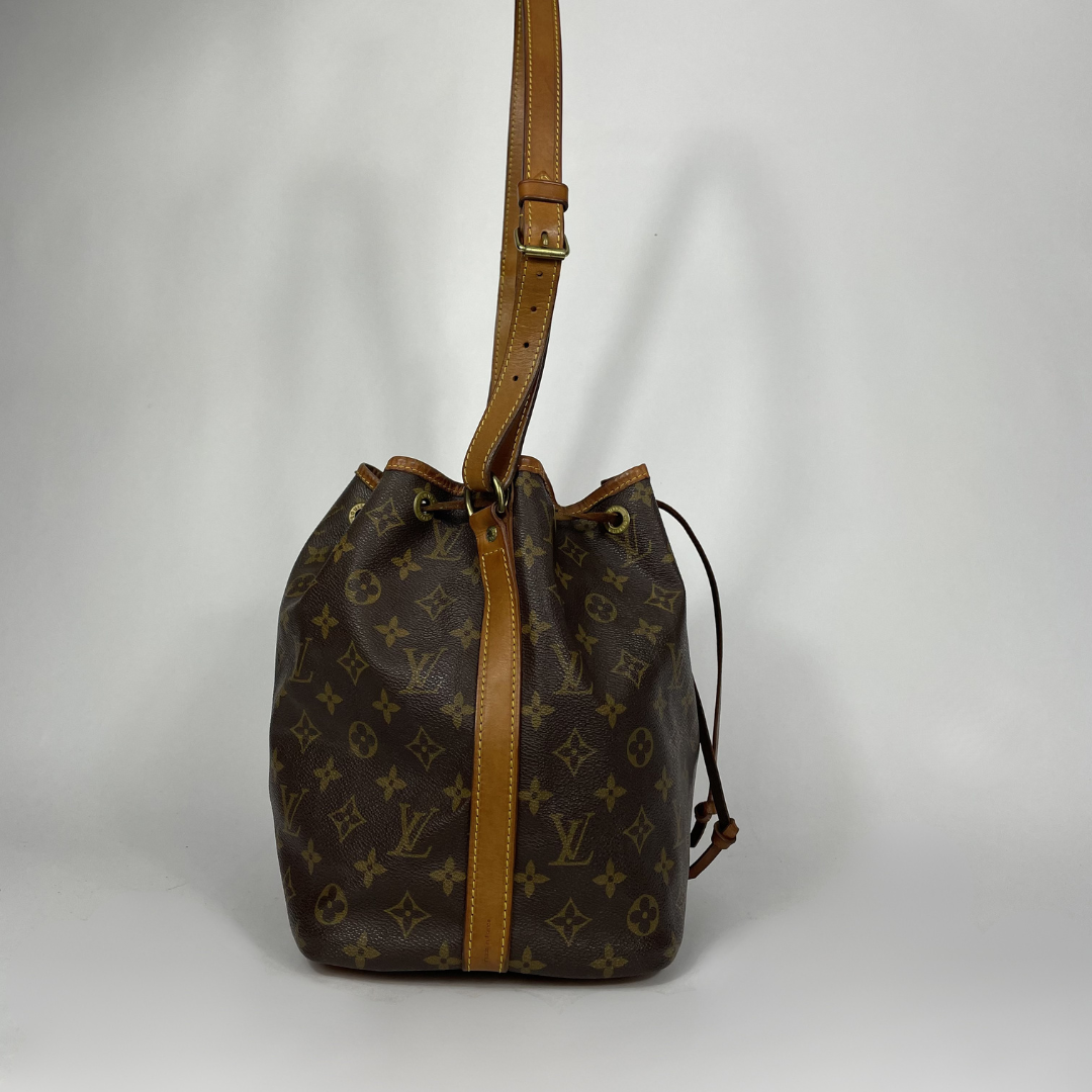 A Louis Vuitton monogram canvas bucket bag with tan leather trim and a single shoulder strap, photographed against a neutral light gray background.