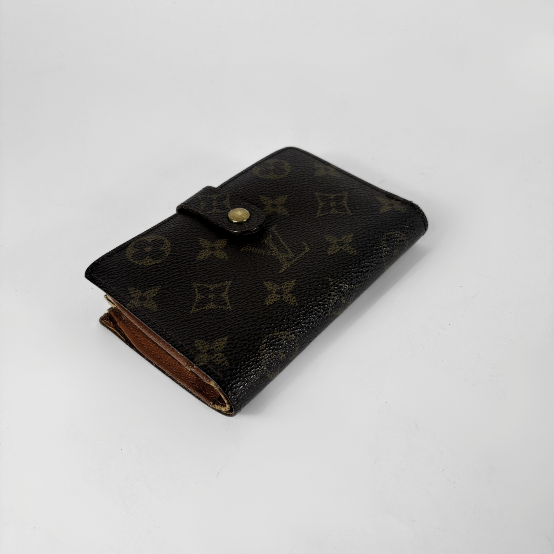 A Louis Vuitton monogram canvas passport holder or small wallet in dark brown with a gold-tone snap button, photographed on a light gray background.