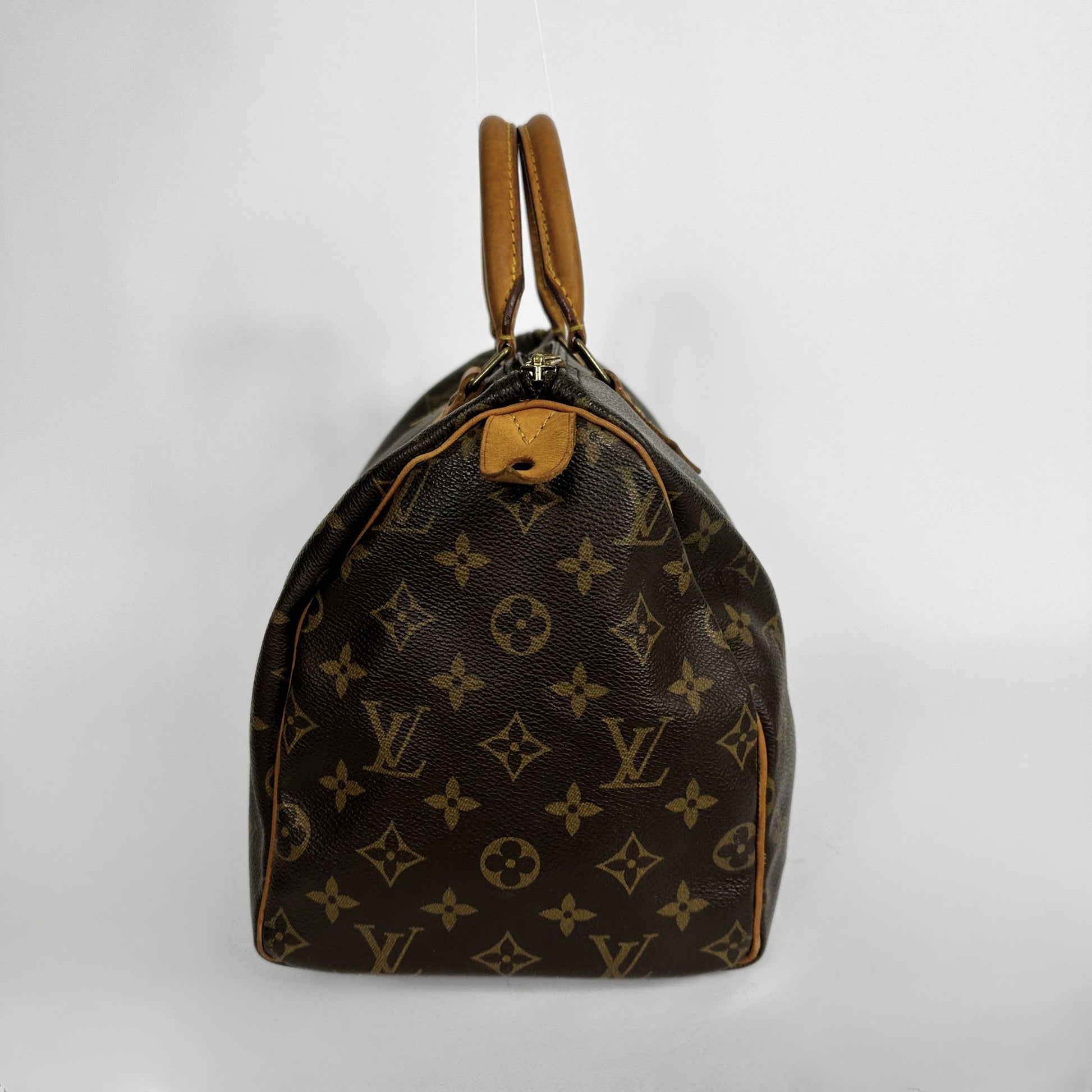 A Louis Vuitton monogram canvas Speedy bag with tan leather handles and trim, photographed against a plain light gray background.