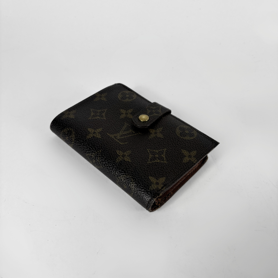 A Louis Vuitton monogram canvas bi-fold wallet in dark brown, featuring a snap-button closure and a small gold-tone button, set against a plain light gray background.