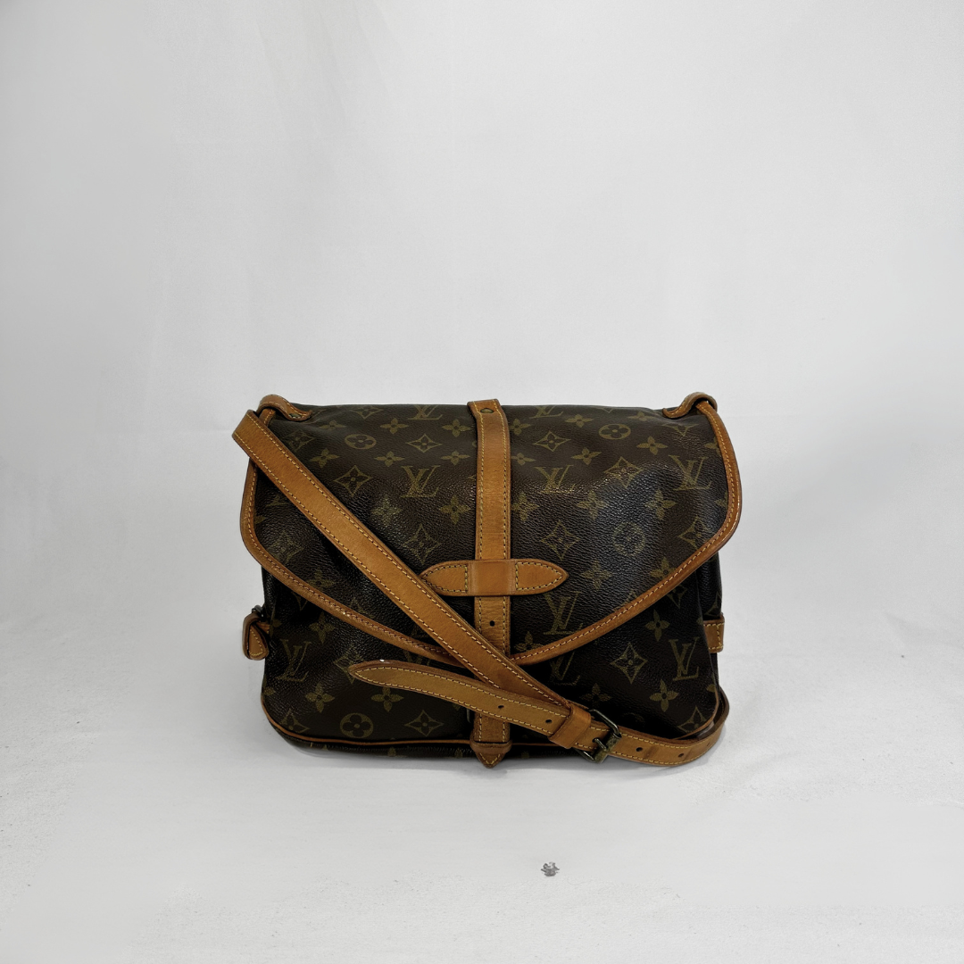 A Louis Vuitton monogram canvas shoulder bag with tan leather trim and strap, photographed against a plain light gray background.