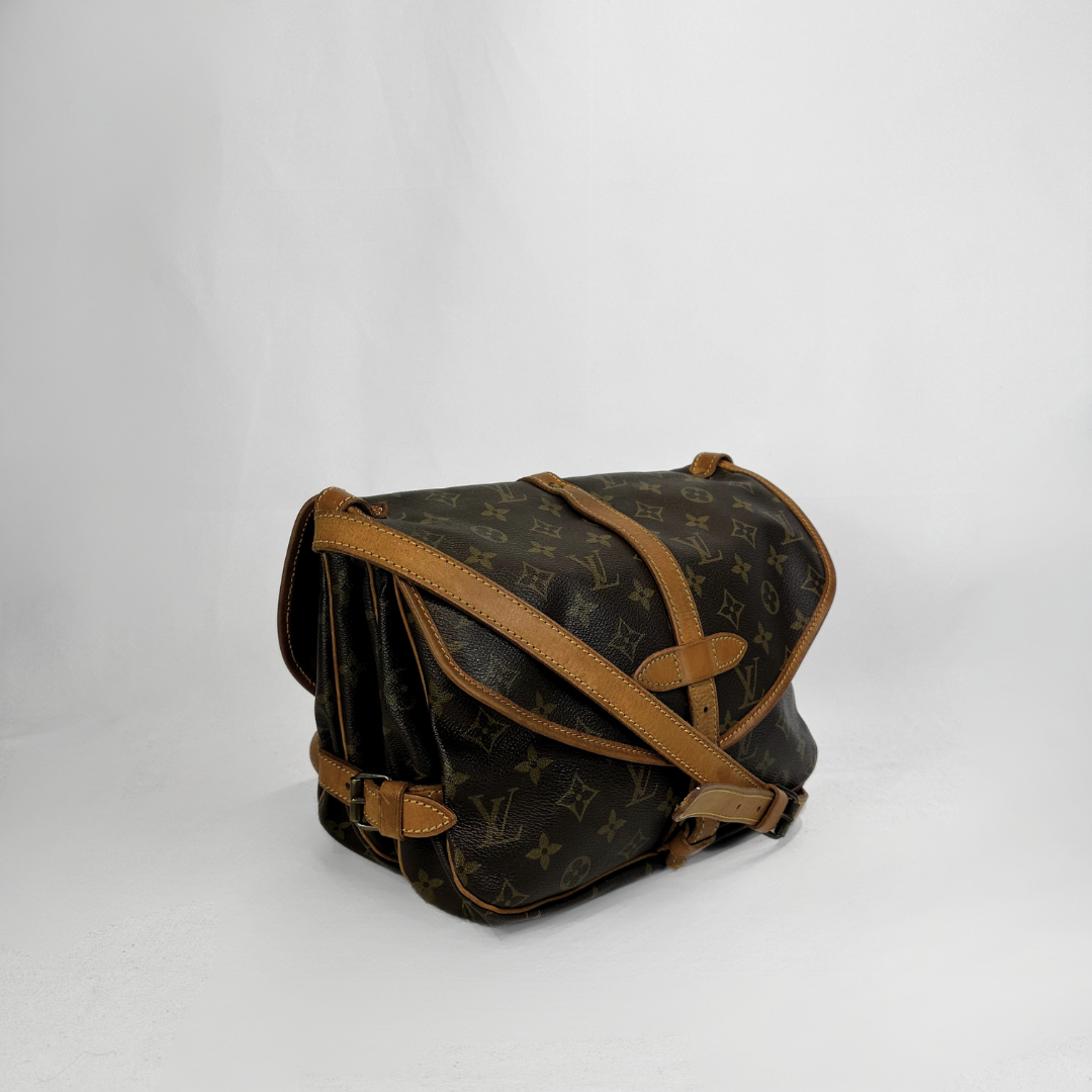 A Louis Vuitton monogram canvas shoulder bag with tan leather trim and strap, photographed on a light gray studio background.