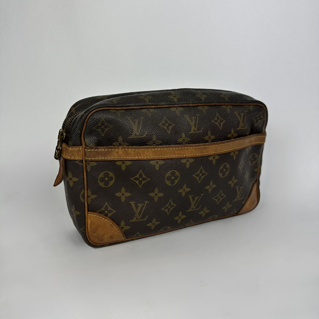 A Louis Vuitton monogram toiletry bag in dark brown coated canvas with tan leather trim and corner patches, shown on a light gray background.