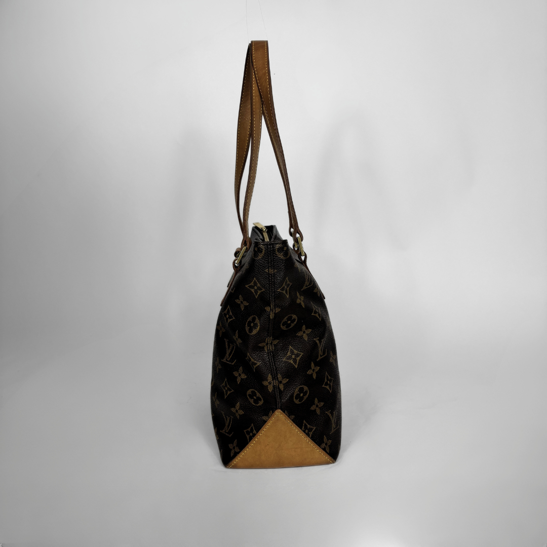 A Louis Vuitton monogram canvas bucket bag with brown leather trim and shoulder strap, standing upright against a light gray background.