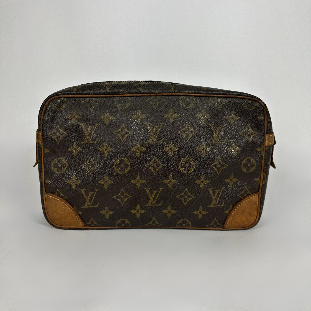 A Louis Vuitton monogram canvas toiletry bag with brown leather corner patches and trim, photographed against a neutral light gray background.