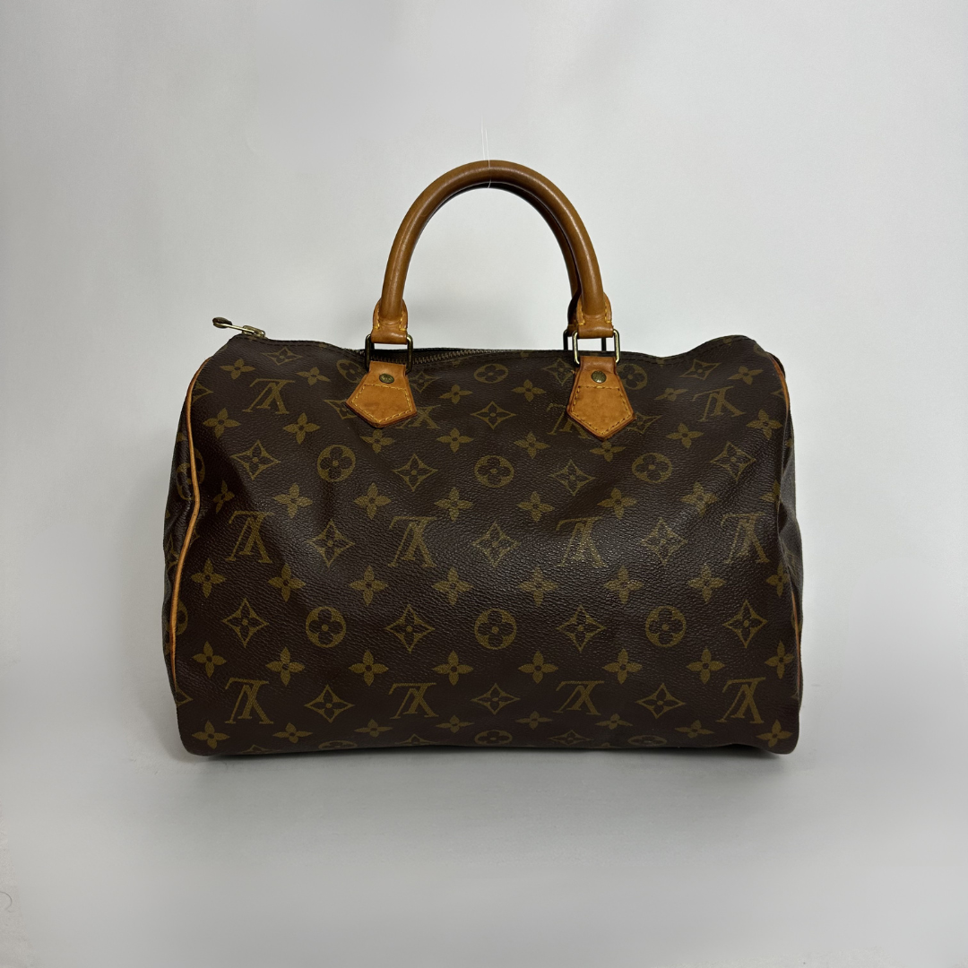 A Louis Vuitton monogram canvas Speedy bag with tan leather handles and trim, photographed against a neutral light gray background.