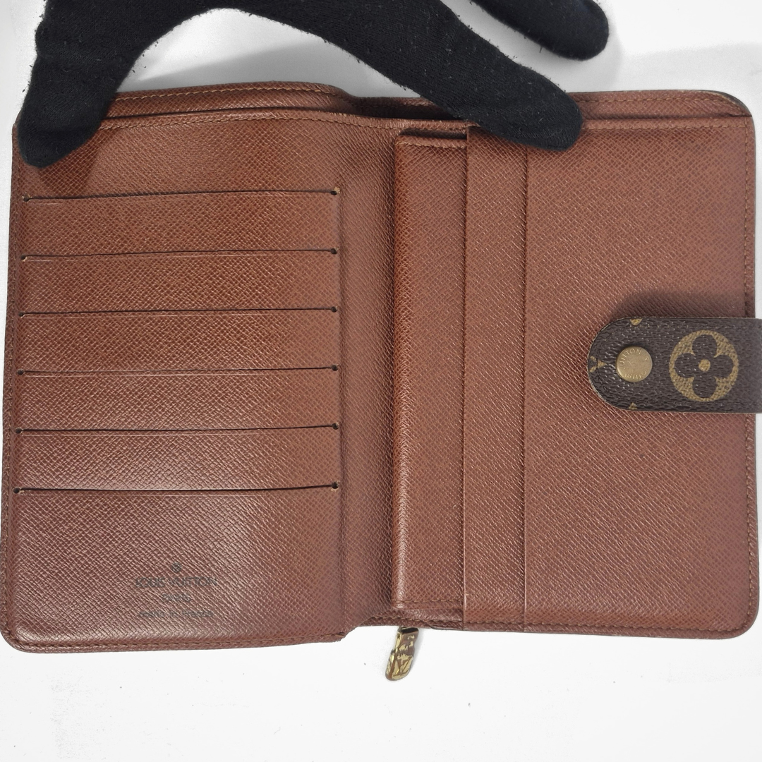 Brown wallet with a gold zipper and brand logo, held open by a black glove.