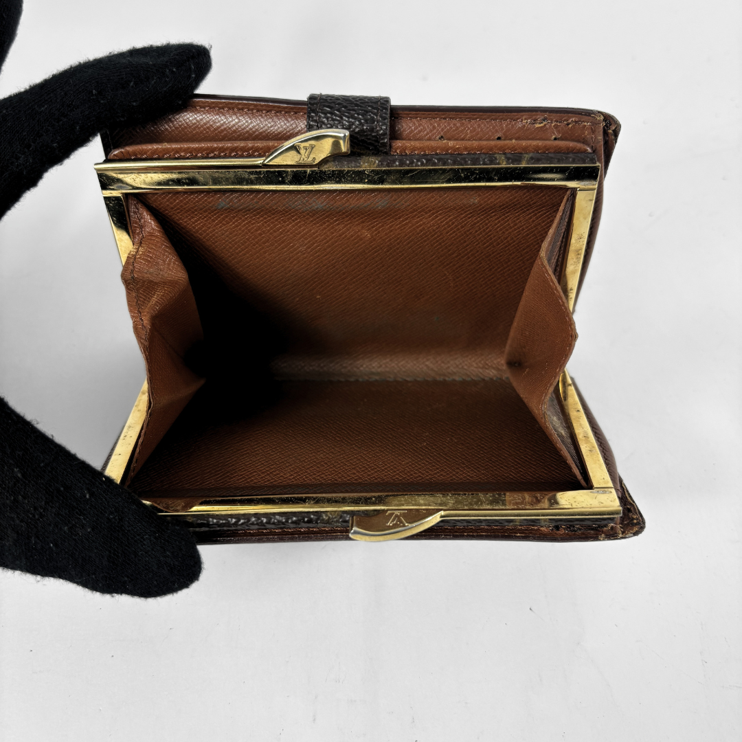 A vintage brown leather coin purse with gold-tone metal frame and a black textured strap, held open by a black gloved hand against a white background.