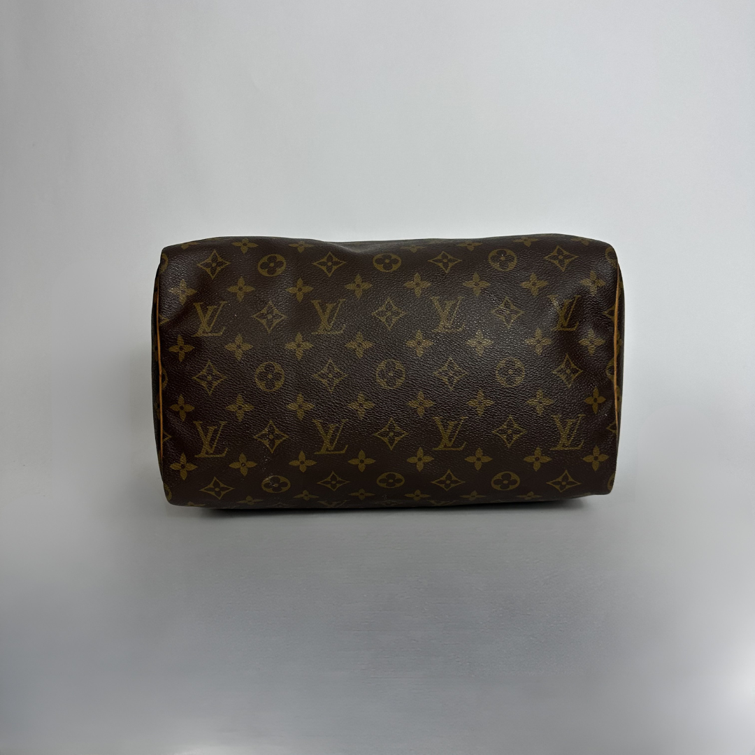 A Louis Vuitton monogram canvas handbag in dark brown with gold-tone monogram motifs, photographed against a neutral gray studio background.