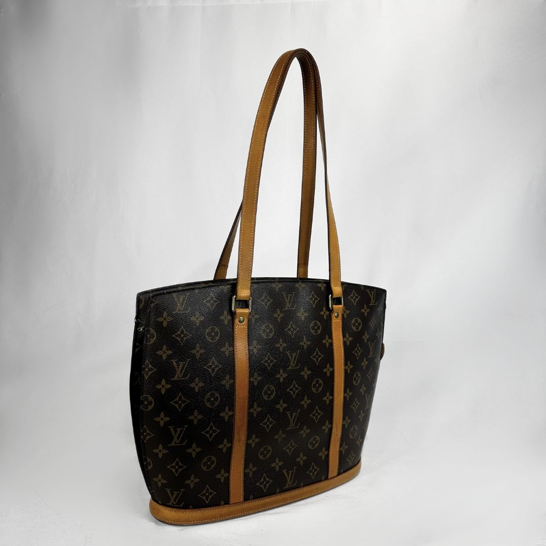 A Louis Vuitton monogram tote bag in dark brown coated canvas with tan leather trim and shoulder straps, shown against a plain light gray background.