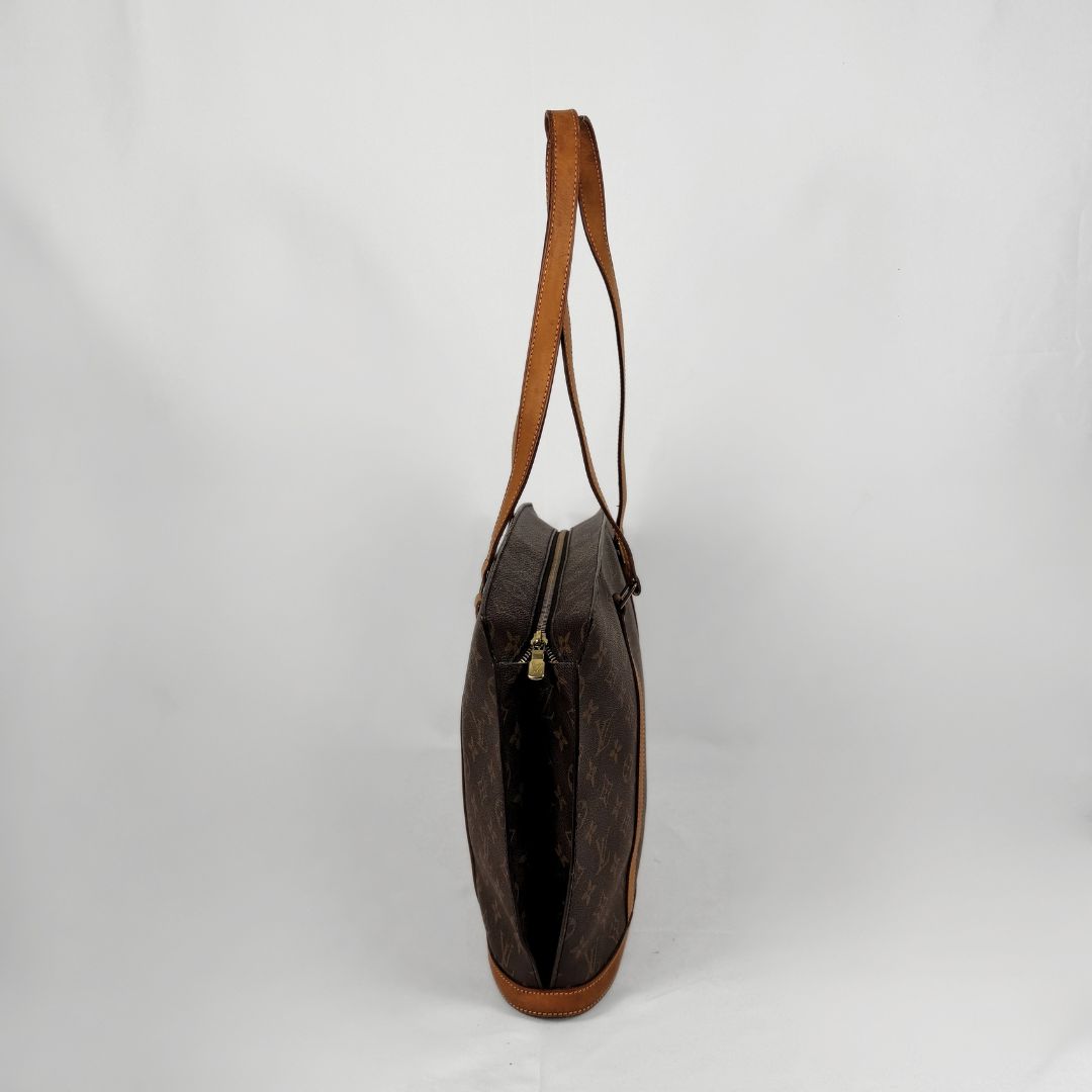 A Louis Vuitton monogram canvas shoulder bag in dark brown with tan leather trim and strap, shown from a side profile view against a white studio background.