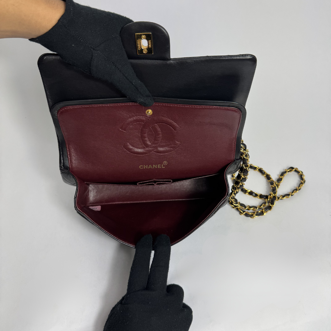Black Chanel handbag with gold chain held by a gloved hand on a white background