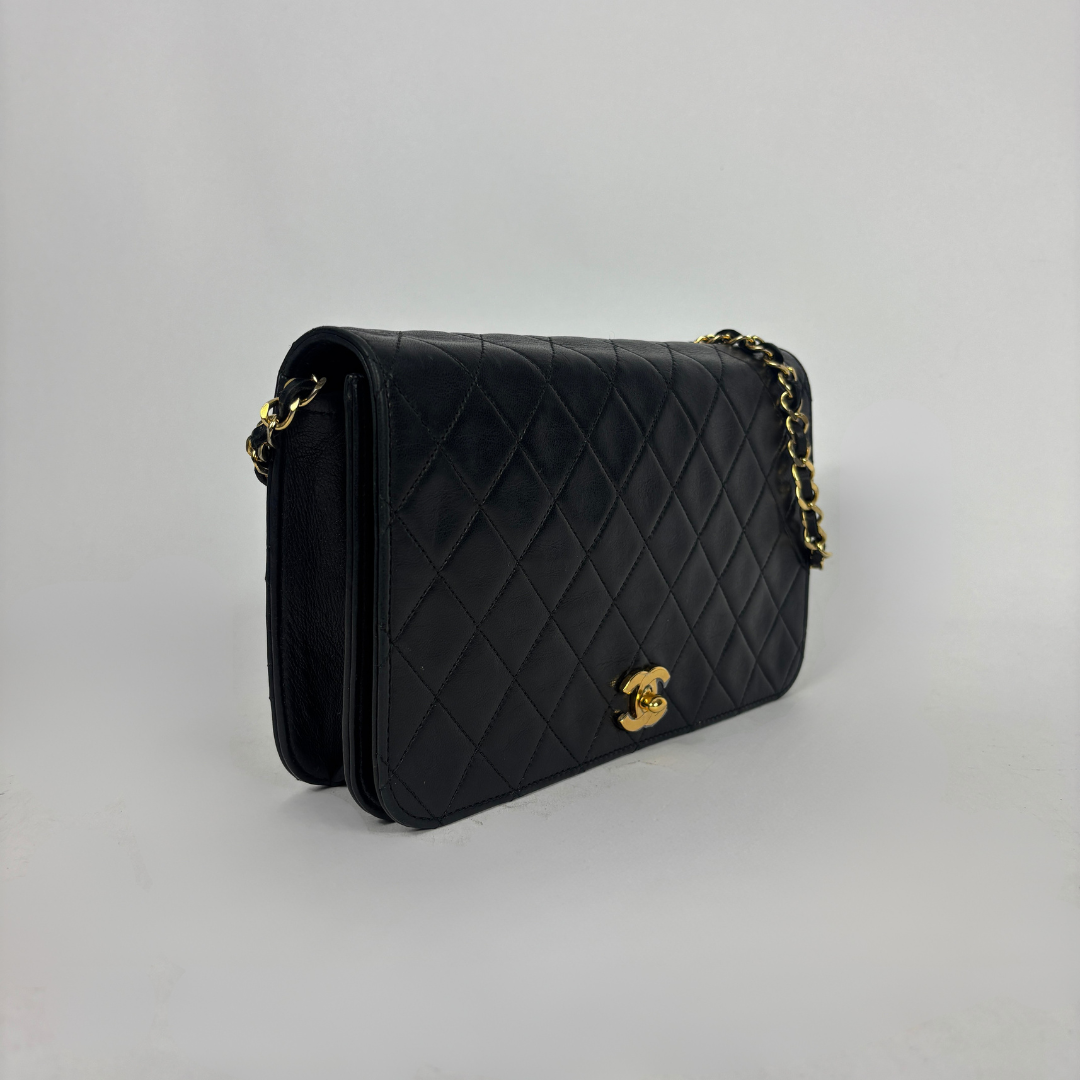 A black quilted leather shoulder bag with gold-tone hardware, featuring a diamond-quilted pattern and a small interlocking CC turn-lock closure on the front flap, photographed against a neutral light gray background.