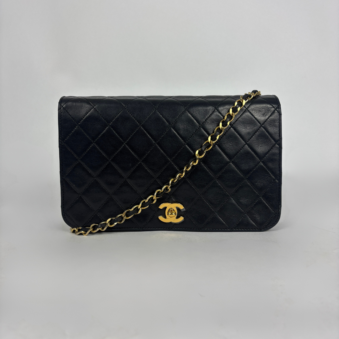 A black quilted leather shoulder bag with a gold-tone chain strap and a gold interlocking CC logo, photographed against a neutral light gray background.