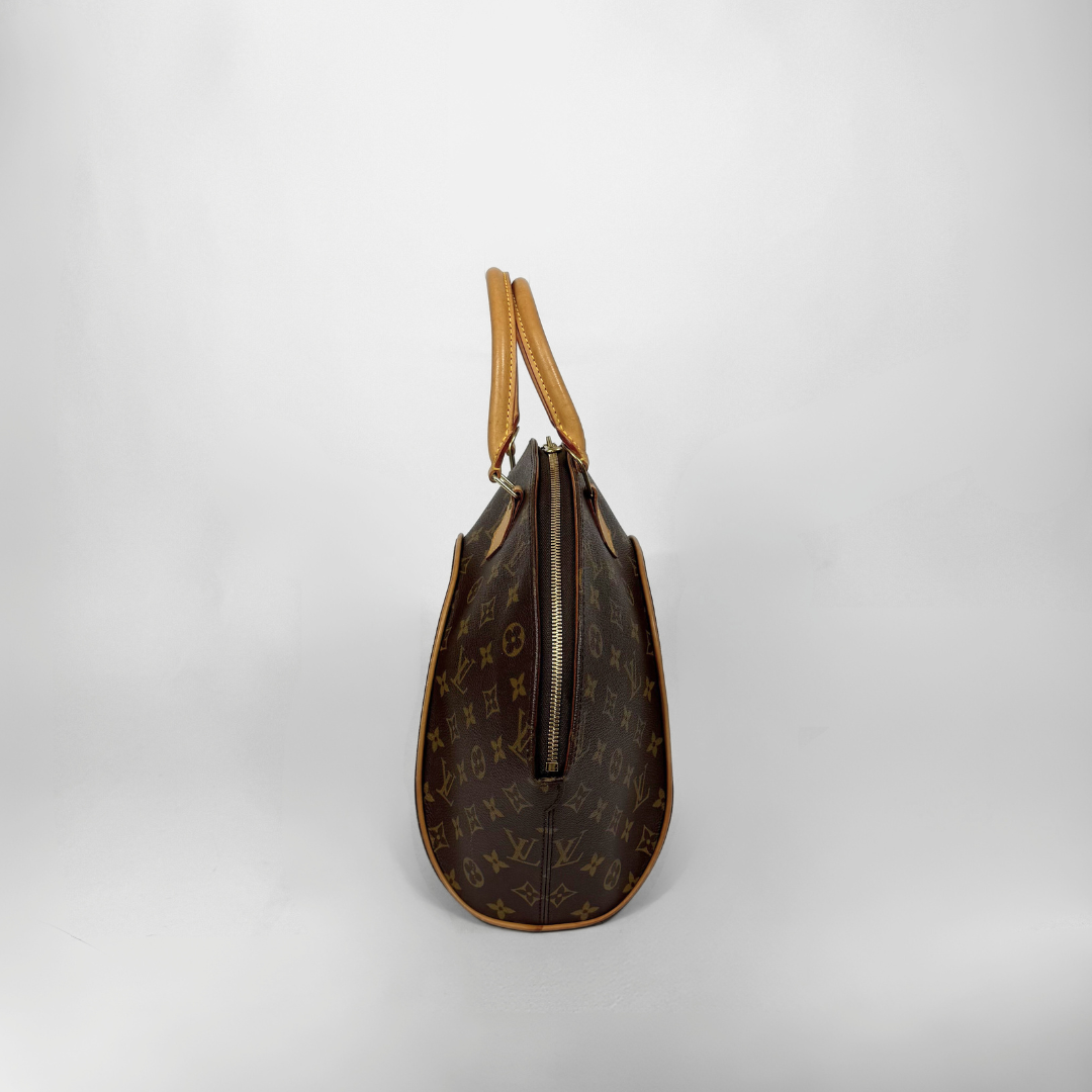 Brown handbag with gold accents held by a gloved hand on a white background