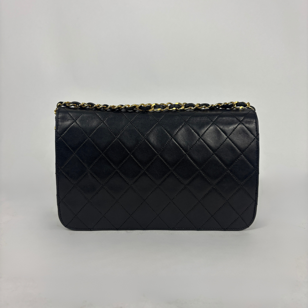 A black quilted leather clutch bag with a gold-tone chain strap, photographed against a neutral light gray background.