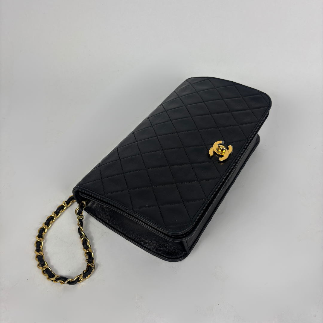 A black quilted leather clutch bag with a gold-tone interlocking CC logo and a gold-and-black chain strap, photographed on a light gray background.