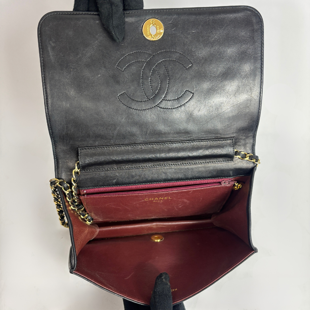 An open Chanel shoulder bag in black leather, showing the interior with a burgundy-red lining, gold-tone chain strap, and the embossed Chanel logo on the inside flap.