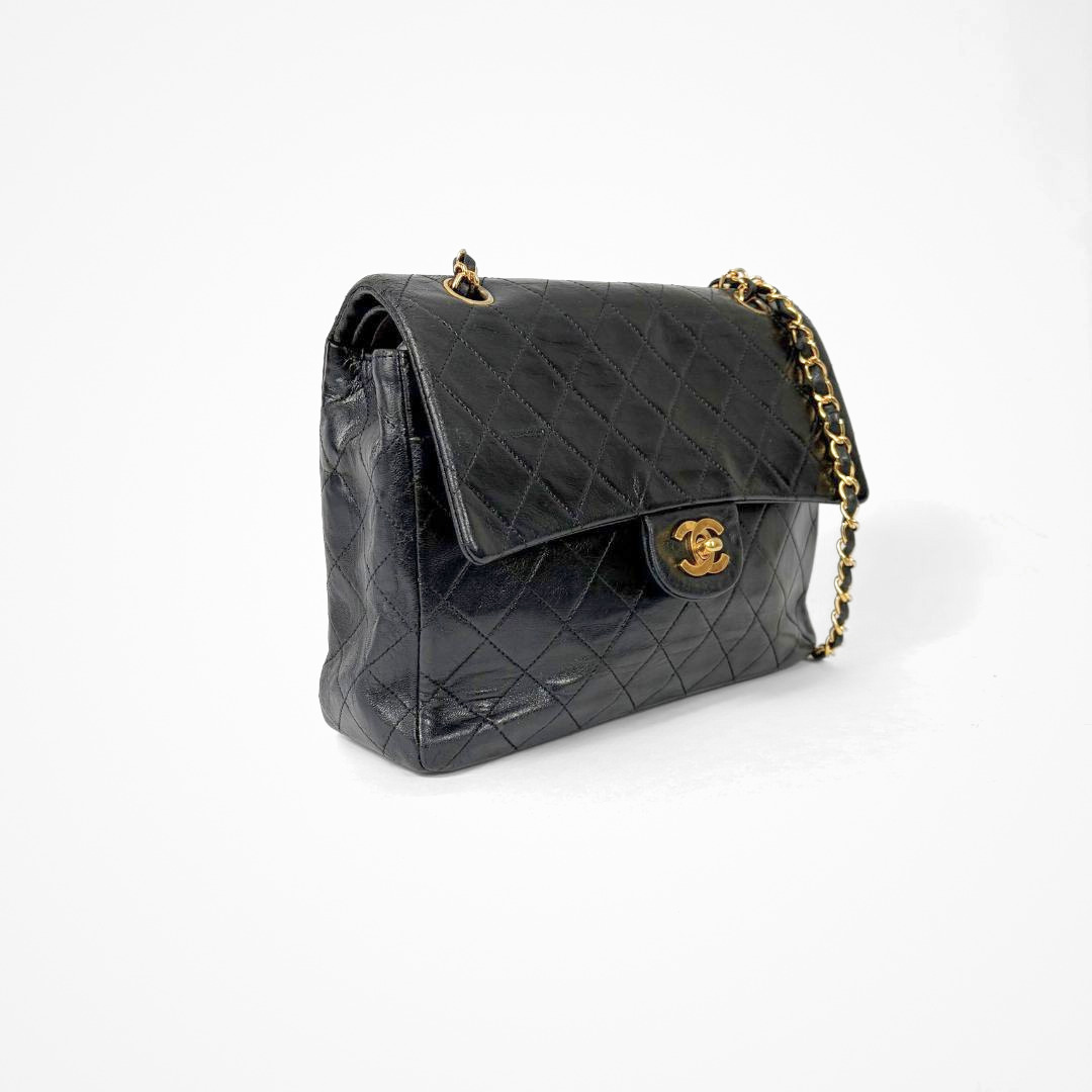 Black Chanel handbag with gold chain and clasp on a white background