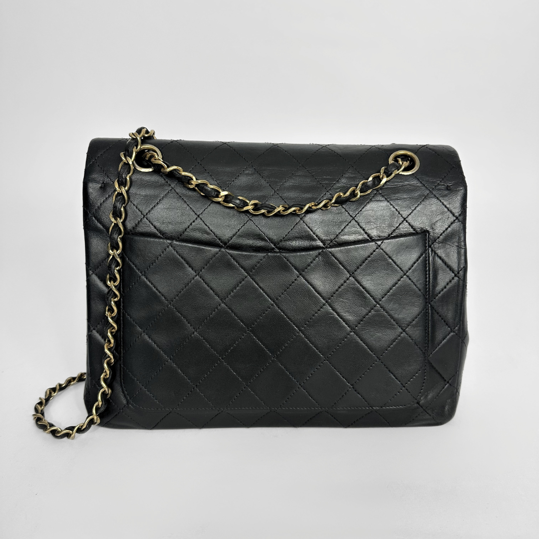 Black quilted handbag with gold chain on a light gray background