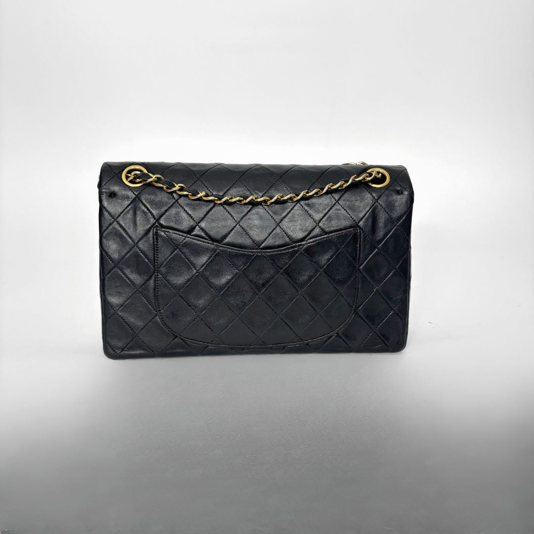 Black quilted handbag with gold chain on a gray background