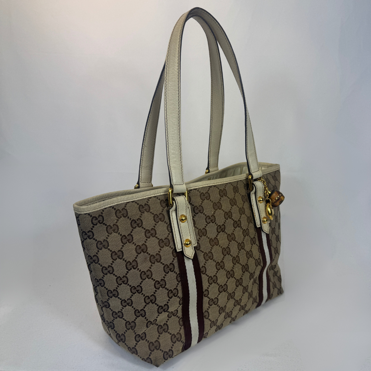 A vintage Gucci tote bag in beige and brown GG Supreme canvas with cream-colored leather handles and trim, featuring gold-tone hardware.