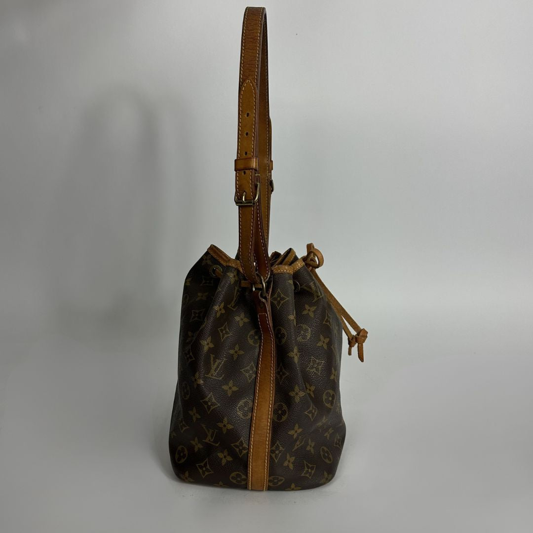 A Louis Vuitton monogram canvas bucket bag with a brown leather shoulder strap and drawstring closure, photographed against a neutral light gray background.