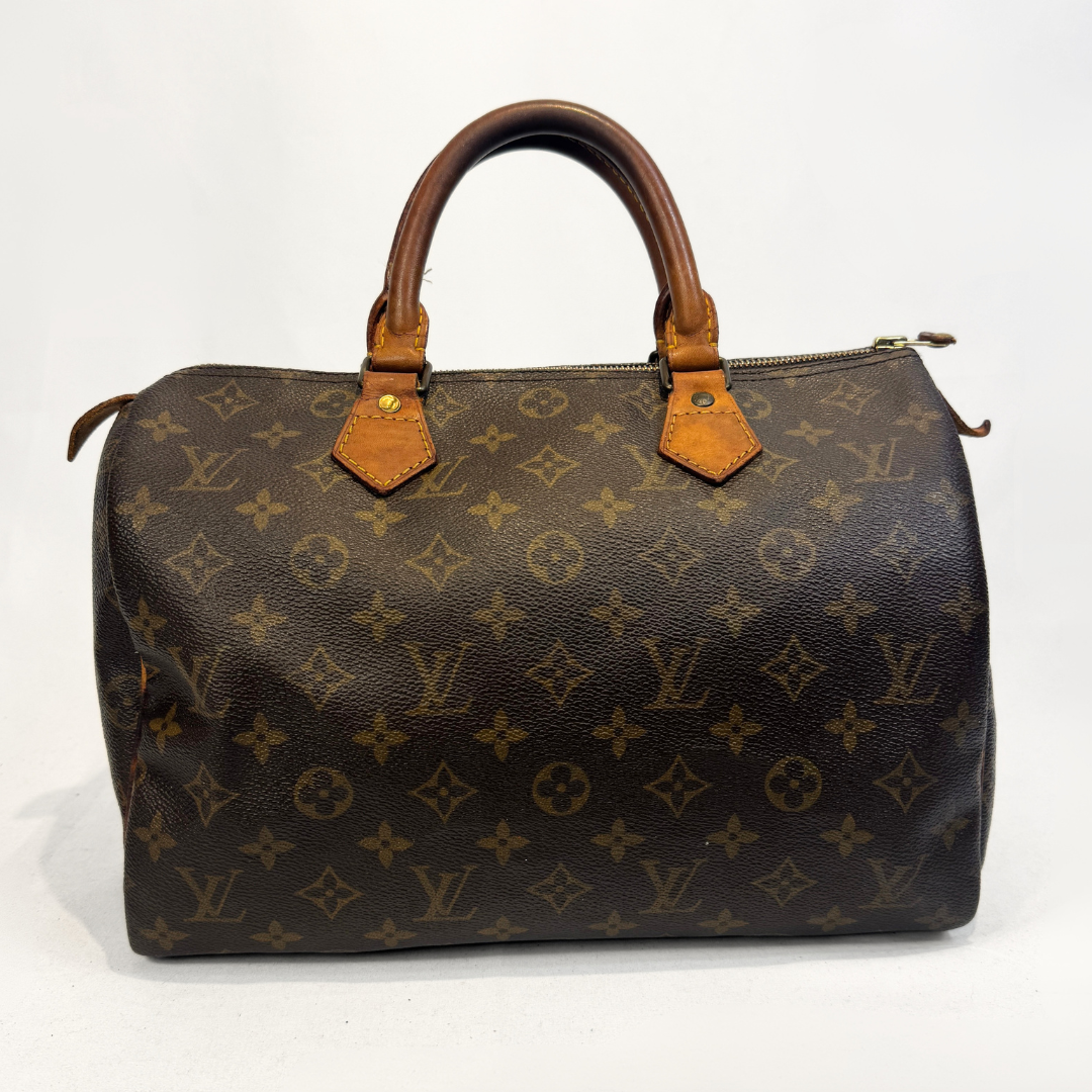 A Louis Vuitton monogram canvas Speedy handbag in dark brown with tan leather handles and trim, photographed against a light gray studio background.