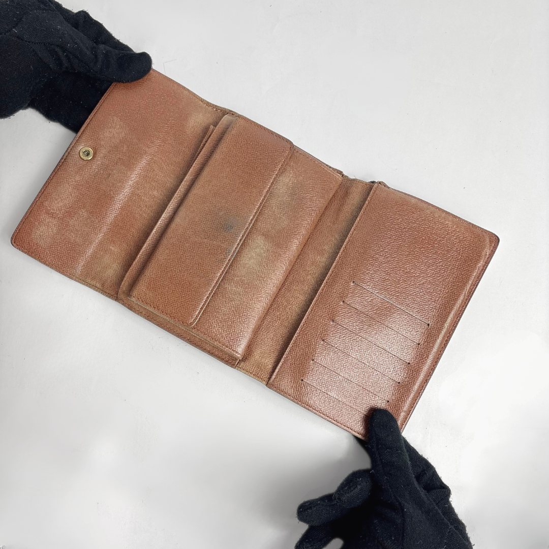 Brown leather wallet held open by black-gloved hands on a white background
