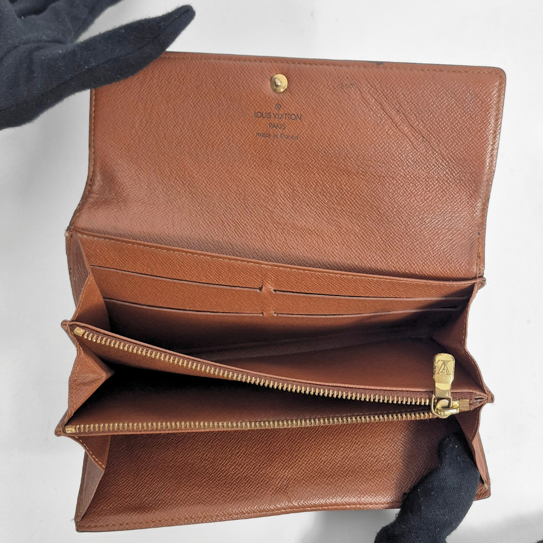 Brown leather wallet with gold zipper held by a gloved hand on a white background