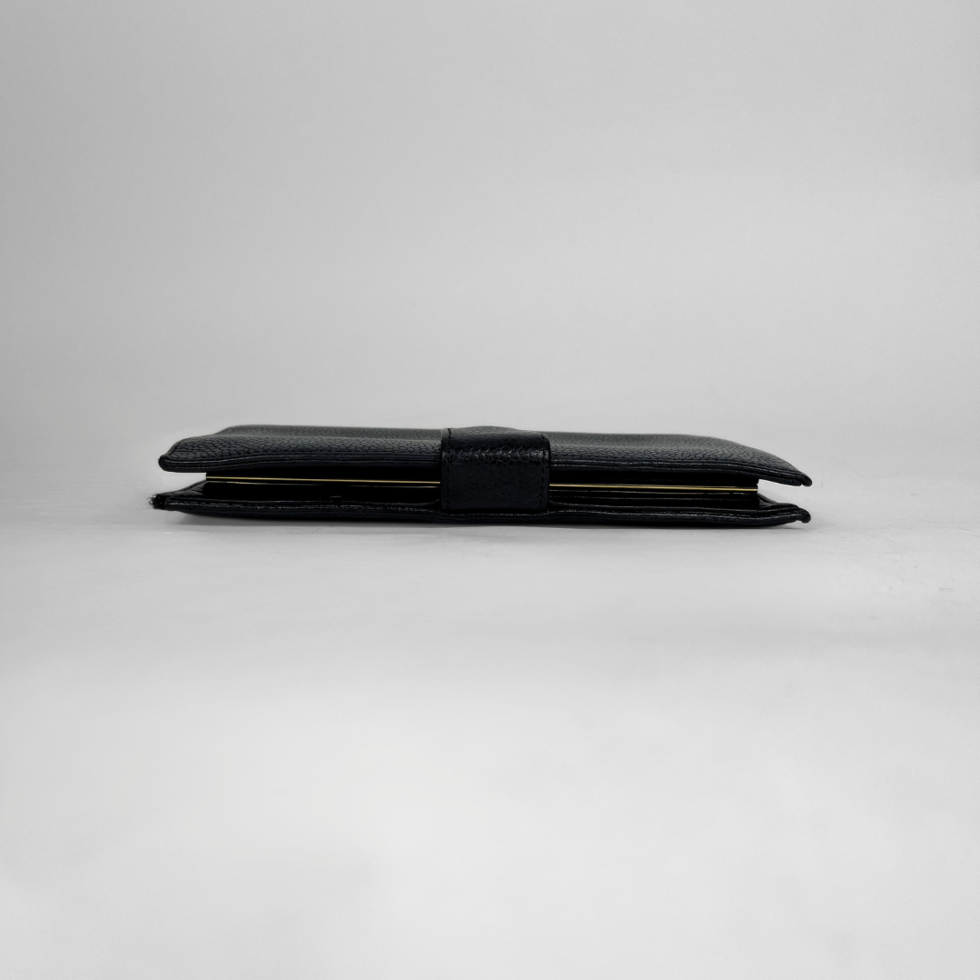 A black textured leather wallet with a matching black strap closure, shown closed on a neutral light gray background.