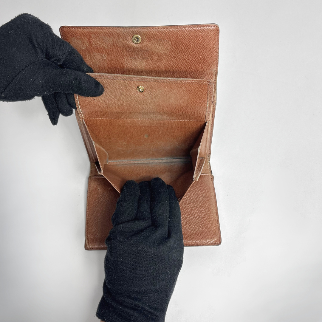 Brown leather wallet being held open by a gloved hand on a white background