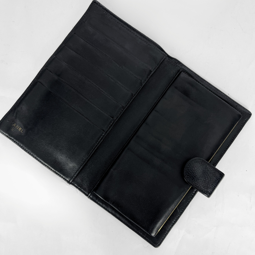 An open black leather wallet or bifold with multiple card slots and a small embossed brand mark on the left panel, photographed on a light neutral background.