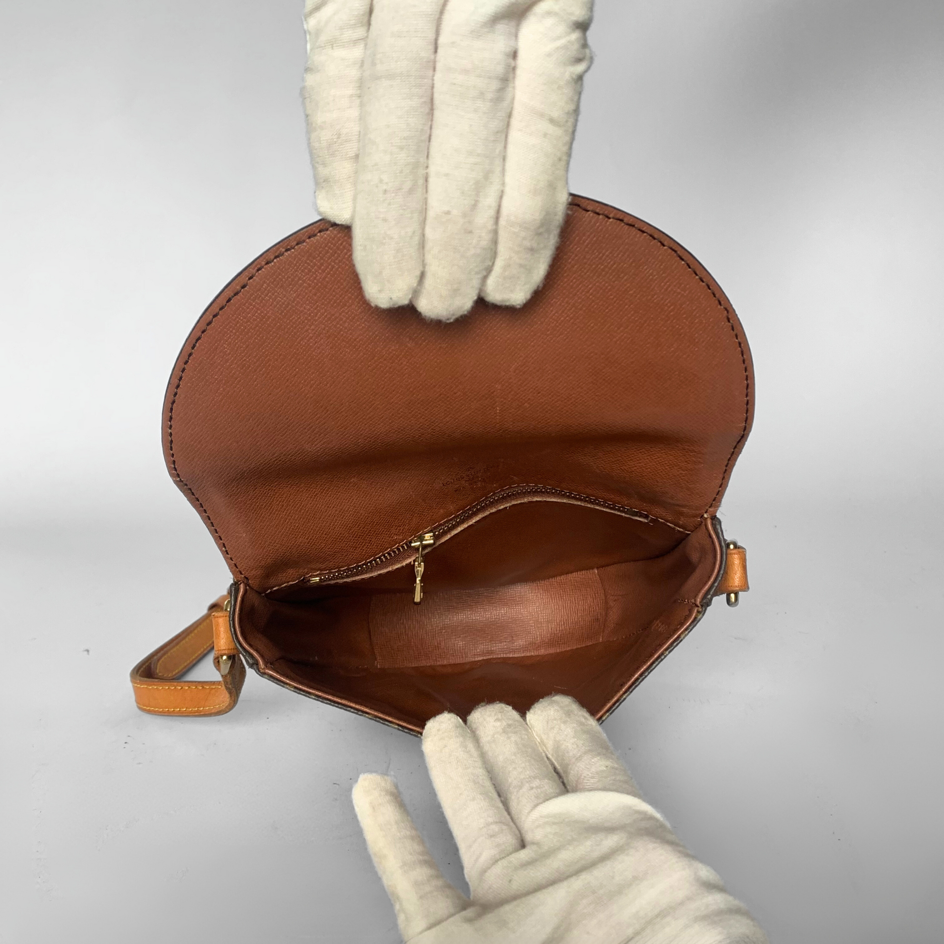 Brown leather handbag held open by a gloved hand on a light gray background