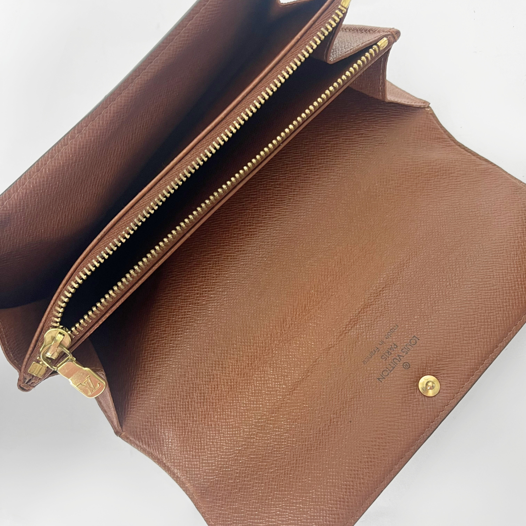 Brown leather clutch bag with gold zipper and hardware on a light gray background