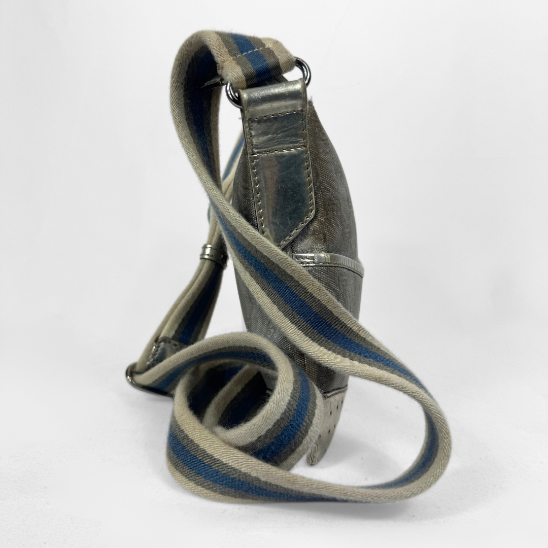 A Gucci GG canvas crossbody bag in metallic silver with a blue and beige striped shoulder strap, silver-tone hardware and a studded base, photographed against a plain white background.