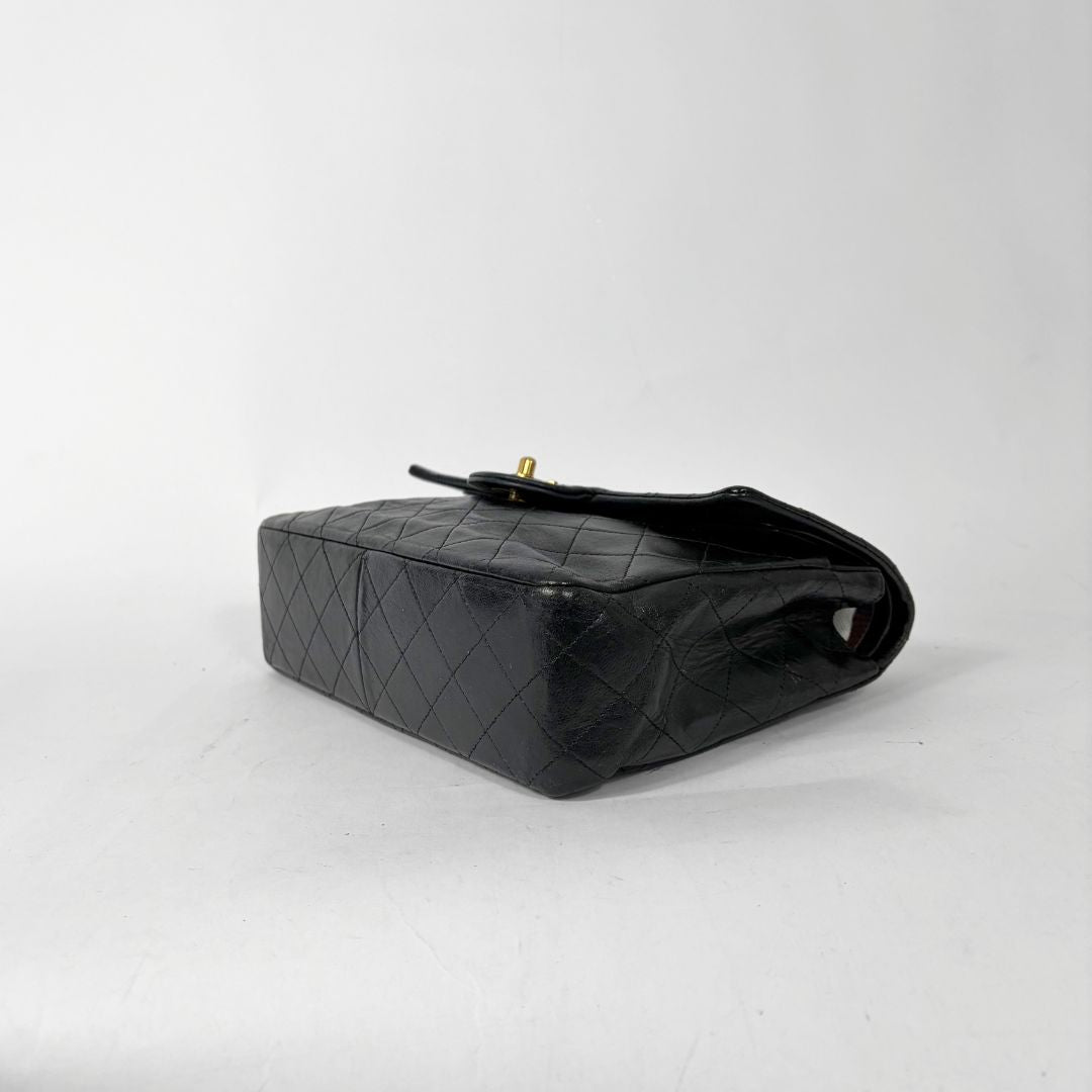 Black quilted handbag with gold chain and clasp on a white background