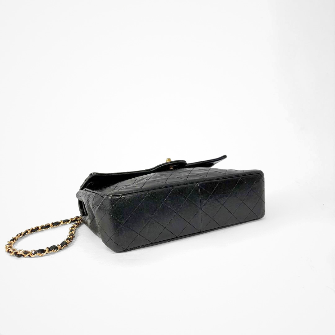 Black Chanel handbag with gold chain and clasp on a white background