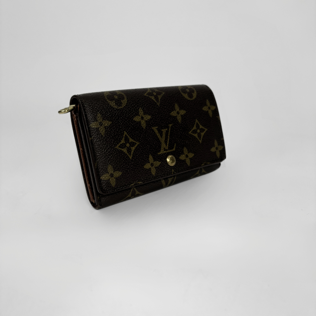 A Louis Vuitton monogram wallet in dark brown coated canvas with gold-tone hardware, photographed on a light gray studio background.