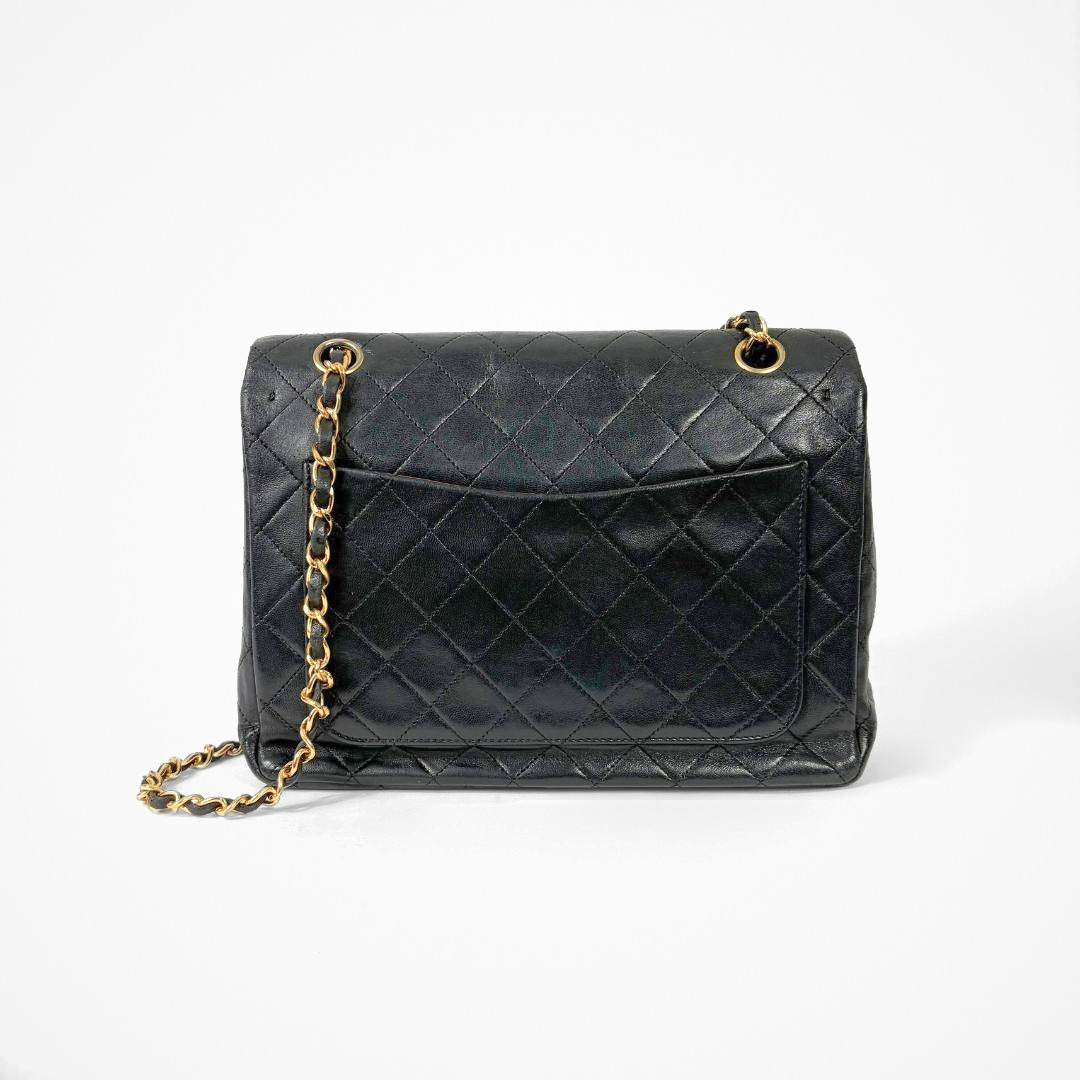 Black Chanel handbag with gold chain and clasp on a white background
