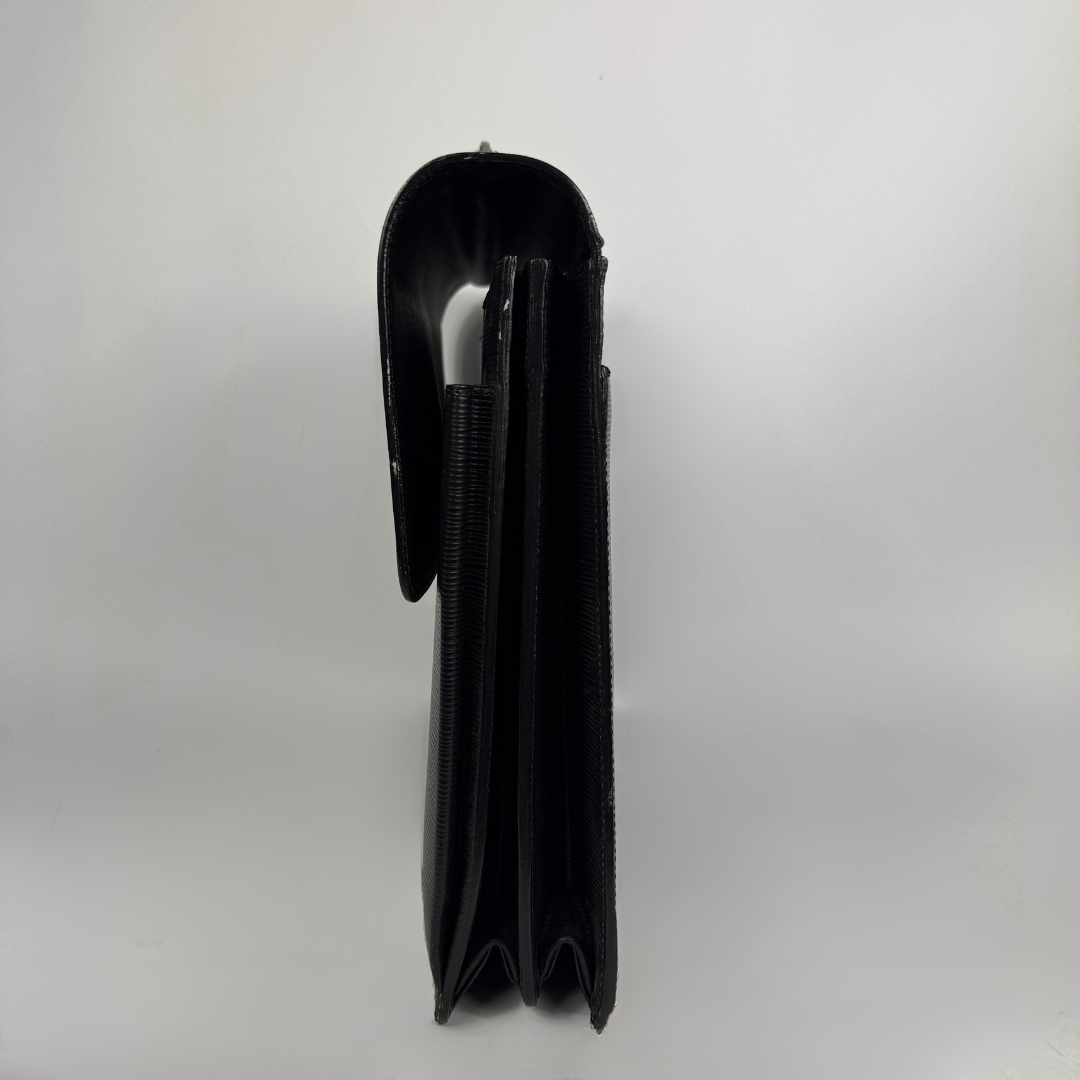 A black leather wallet shown from the side profile, featuring a smooth leather flap and a textured elastic band, set against a plain light gray background.