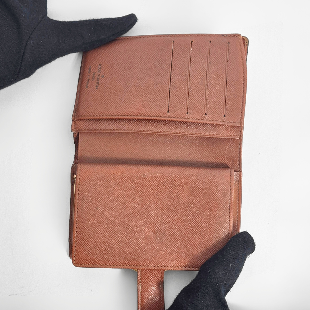 Brown textured wallet held by a gloved hand on a white background